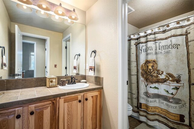 bathroom with tile patterned floors, walk in shower, vanity, a textured ceiling, and toilet