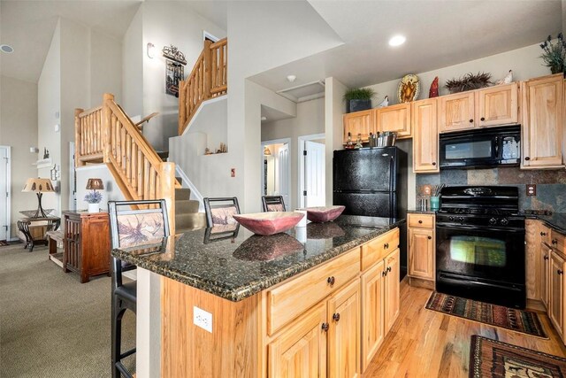 kitchen with a breakfast bar, a center island, backsplash, dark stone counters, and black appliances