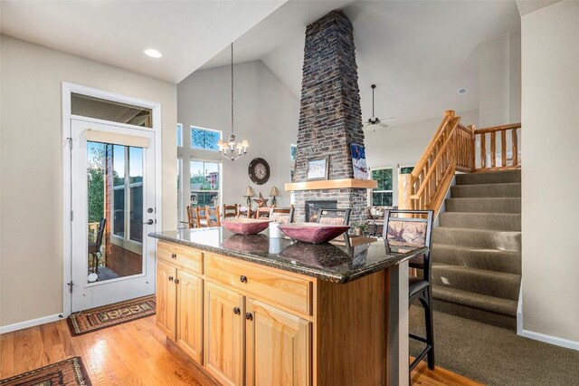 kitchen with a center island, dark stone countertops, decorative light fixtures, a fireplace, and ceiling fan with notable chandelier