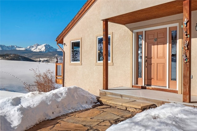 snow covered property entrance with a mountain view and stucco siding