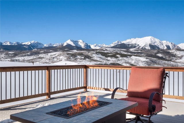 snow covered deck featuring a mountain view and a fire pit