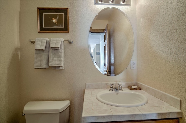 half bathroom with toilet, vanity, and a textured wall