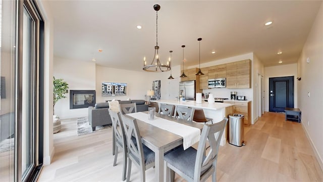 dining area with light wood-type flooring, a glass covered fireplace, a notable chandelier, and recessed lighting