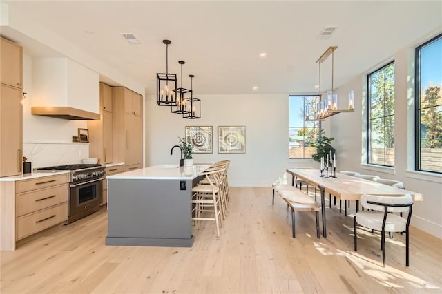 kitchen featuring stainless steel stove, a kitchen island with sink, pendant lighting, and an inviting chandelier