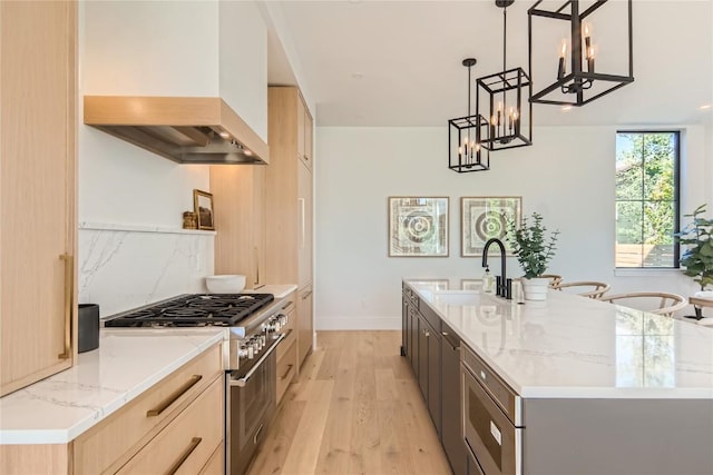 kitchen with an island with sink, custom exhaust hood, high end range, and decorative light fixtures