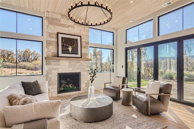 interior space featuring a notable chandelier, a stone fireplace, a towering ceiling, wood ceiling, and hardwood / wood-style floors