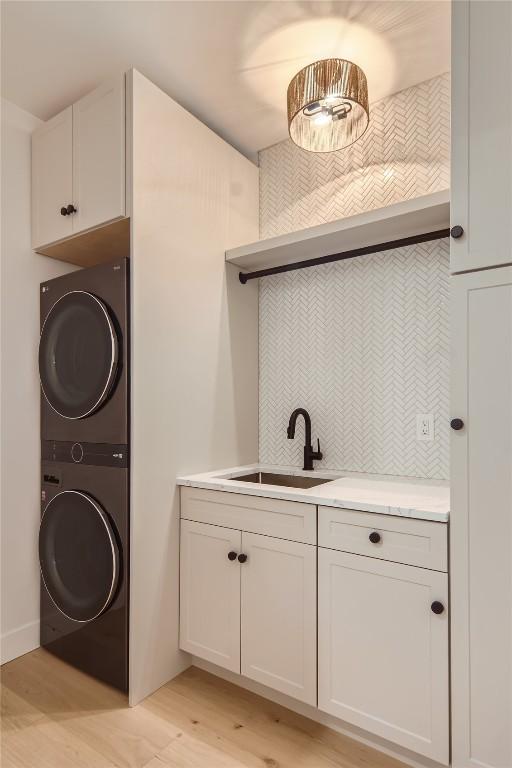 clothes washing area with sink, stacked washing maching and dryer, cabinets, and light hardwood / wood-style flooring