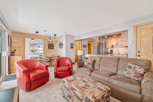 living room featuring sink, a healthy amount of sunlight, light colored carpet, and wood walls