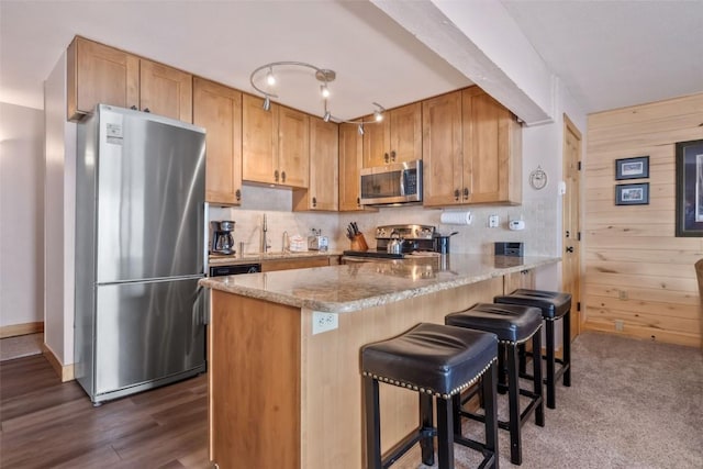 kitchen with light stone counters, stainless steel appliances, wooden walls, and kitchen peninsula