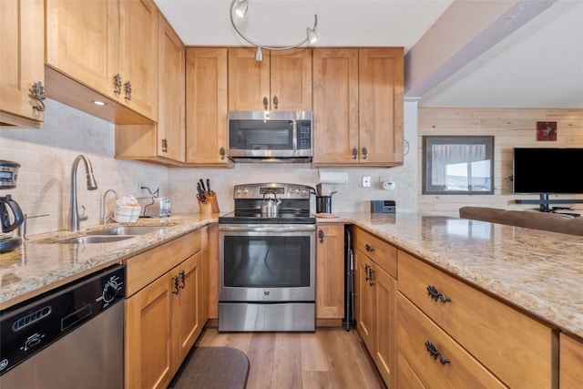 kitchen featuring stainless steel appliances, sink, light stone counters, and light hardwood / wood-style floors