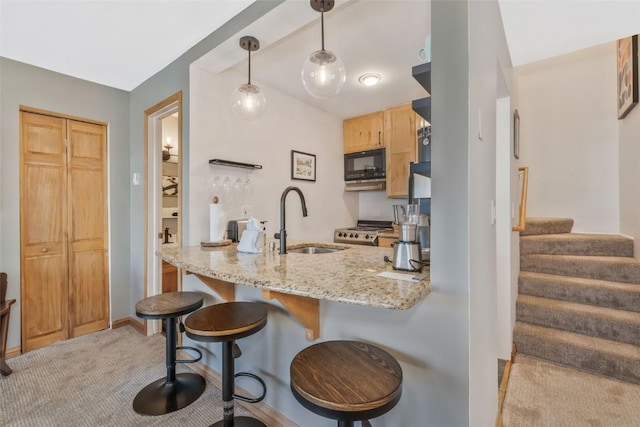 kitchen with a breakfast bar area, light stone counters, a peninsula, black microwave, and a sink