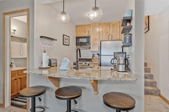 kitchen featuring a breakfast bar, freestanding refrigerator, a peninsula, light brown cabinets, and black microwave