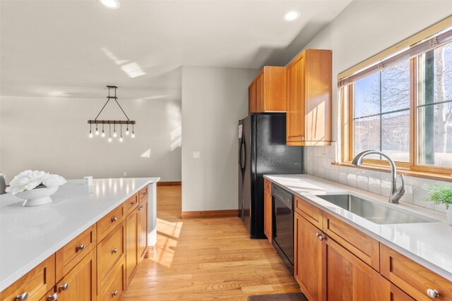 kitchen featuring decorative backsplash, dishwasher, brown cabinetry, light wood-type flooring, and a sink