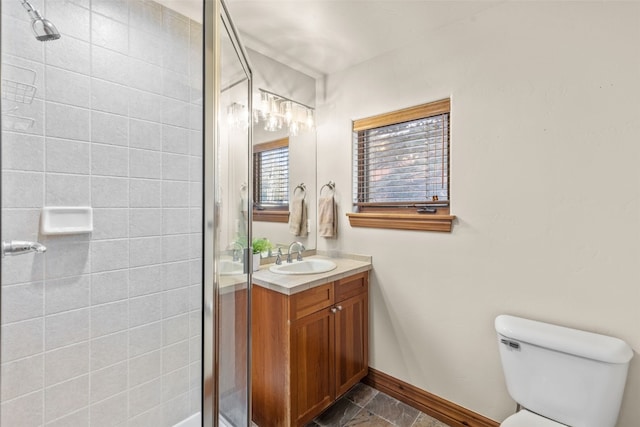 bathroom with toilet, vanity, a stall shower, baseboards, and stone finish floor