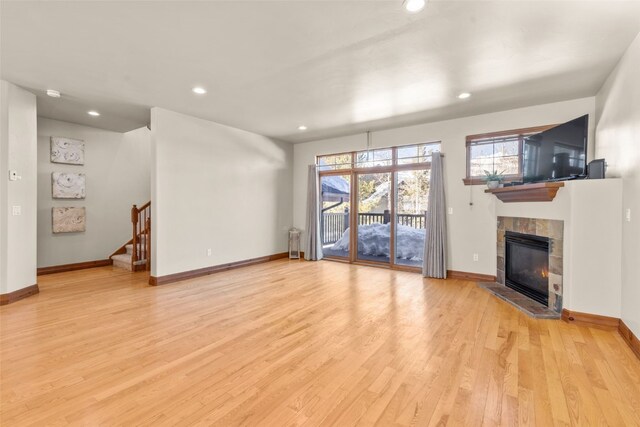 unfurnished living room featuring stairway, a tiled fireplace, light wood-style flooring, and baseboards