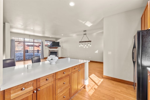 kitchen featuring a tile fireplace, open floor plan, light countertops, freestanding refrigerator, and light wood finished floors