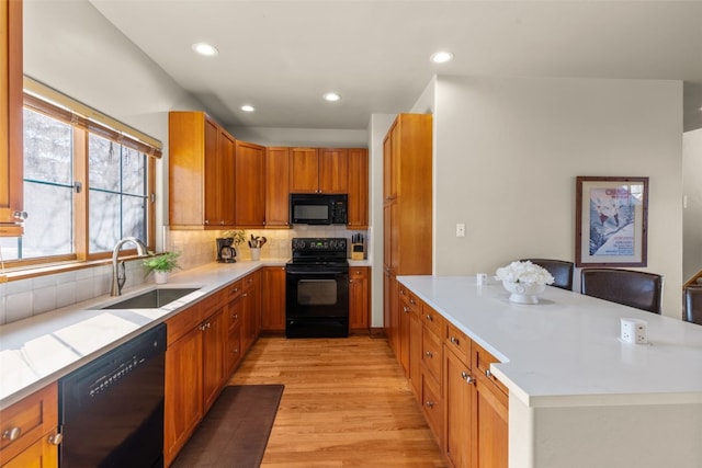 kitchen with light wood finished floors, tasteful backsplash, light countertops, black appliances, and a sink