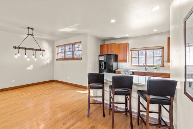 kitchen featuring decorative backsplash, a kitchen breakfast bar, black refrigerator with ice dispenser, light countertops, and light wood-type flooring