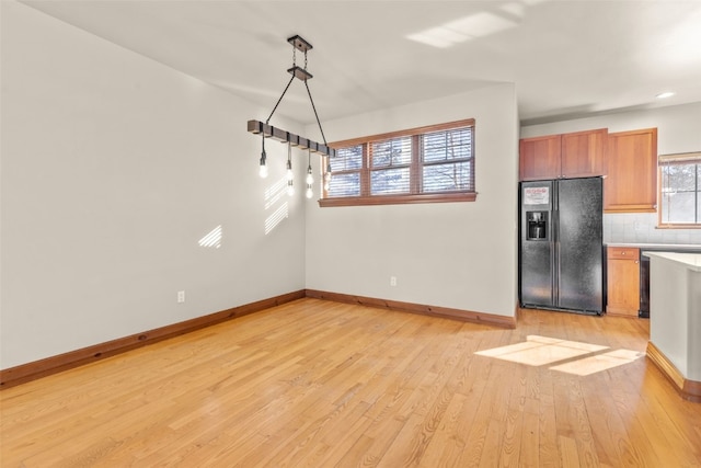 kitchen featuring black fridge with ice dispenser, baseboards, light wood-style floors, decorative backsplash, and brown cabinetry