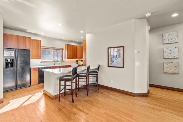 kitchen featuring decorative backsplash, light wood-style flooring, a kitchen breakfast bar, light countertops, and black appliances