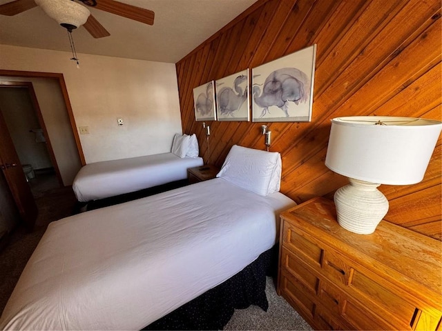 carpeted bedroom featuring a ceiling fan and wood walls