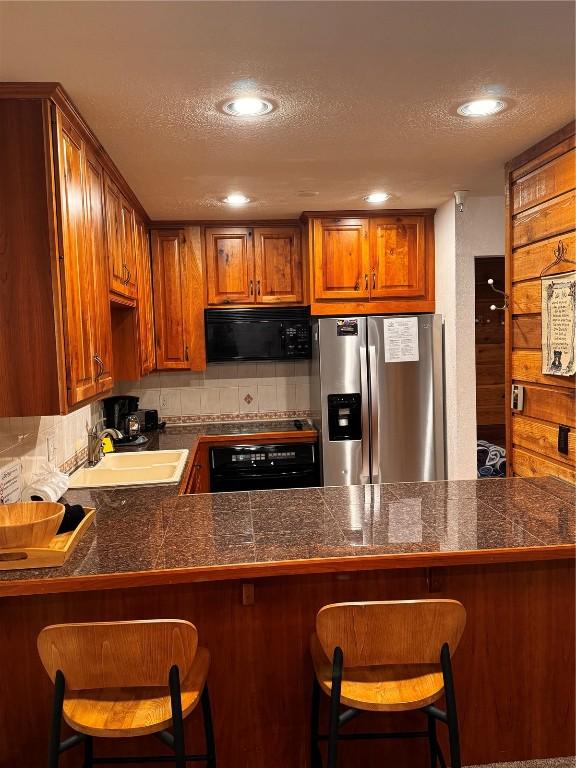 kitchen with brown cabinets, tile countertops, a sink, a textured ceiling, and black appliances