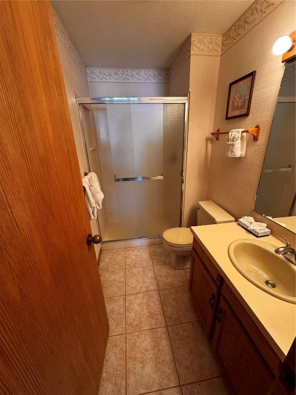 full bathroom featuring a stall shower, toilet, tile patterned floors, a textured ceiling, and vanity