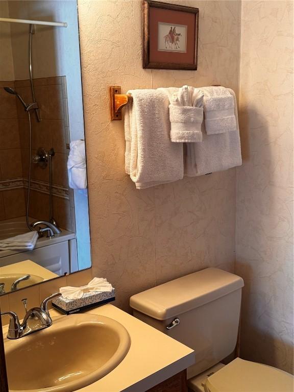 bathroom with toilet, a textured wall, a shower, and vanity