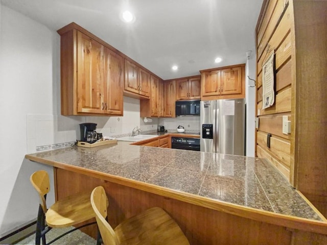 kitchen with tile counters, brown cabinets, black microwave, stainless steel refrigerator with ice dispenser, and recessed lighting