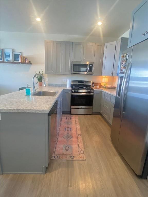 kitchen with a sink, appliances with stainless steel finishes, light wood-style flooring, and gray cabinets