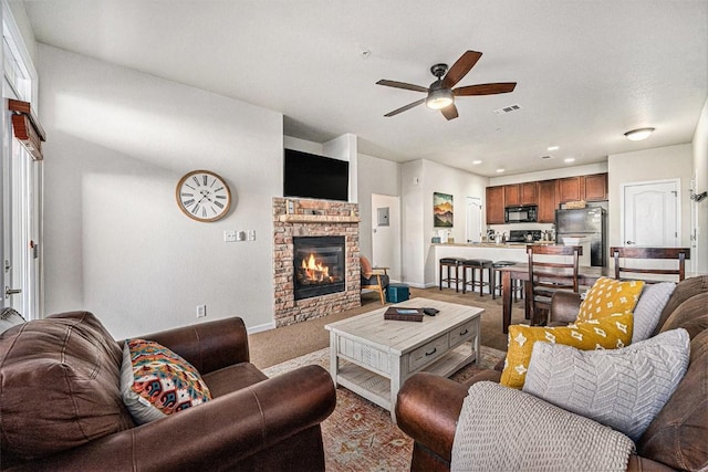 living room with a stone fireplace, light carpet, visible vents, baseboards, and a ceiling fan