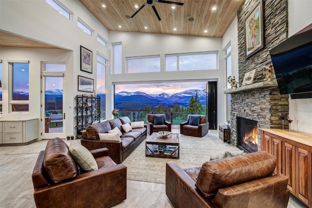 living room featuring ceiling fan, wood ceiling, a fireplace, and a towering ceiling