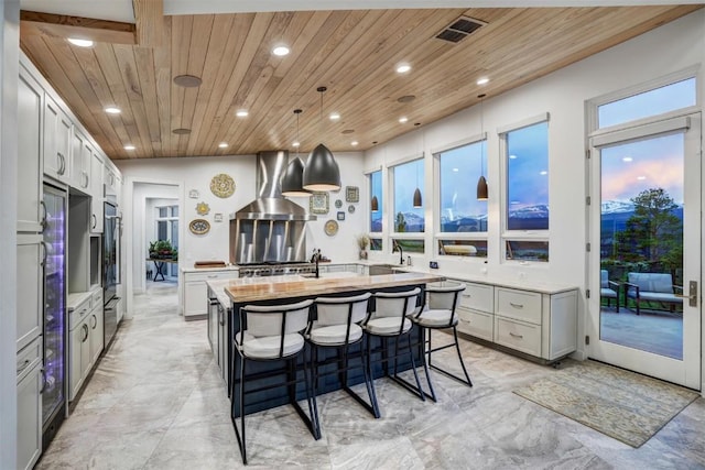 kitchen with island range hood, a center island with sink, wood ceiling, and decorative light fixtures