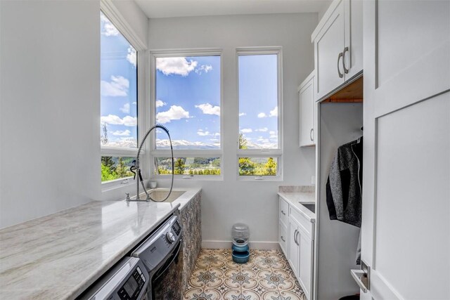 kitchen featuring light stone countertops, sink, light tile patterned floors, white cabinets, and washing machine and dryer