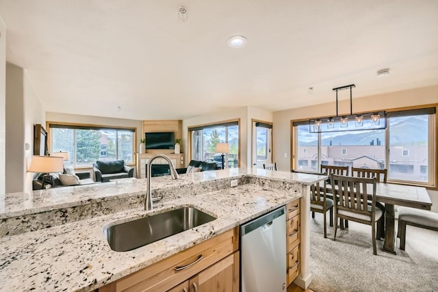 kitchen featuring light colored carpet, open floor plan, light stone countertops, stainless steel dishwasher, and a sink