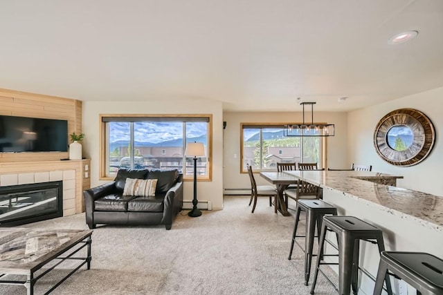 living area with light carpet, baseboard heating, a tiled fireplace, and a wealth of natural light