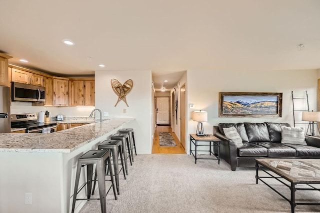 kitchen with light colored carpet, stainless steel appliances, a peninsula, a kitchen breakfast bar, and light stone countertops