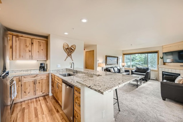 kitchen featuring a peninsula, a sink, open floor plan, appliances with stainless steel finishes, and light brown cabinetry