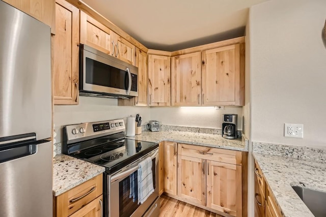 kitchen with stainless steel appliances, light brown cabinetry, light wood-type flooring, and light stone countertops