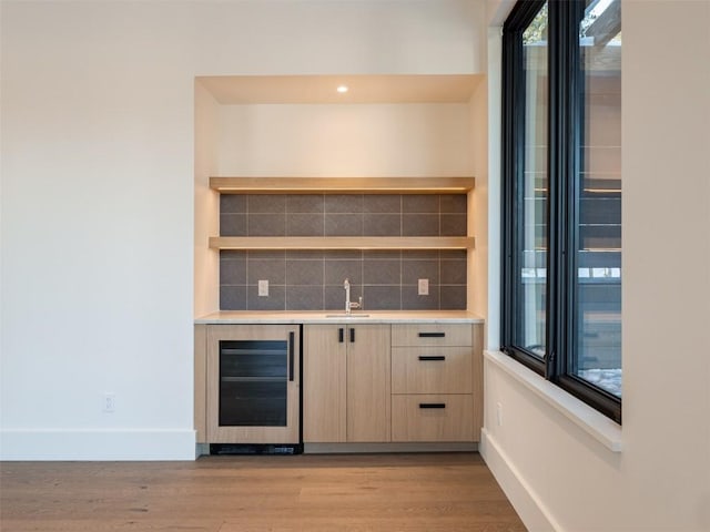 bar featuring light brown cabinetry, tasteful backsplash, sink, light hardwood / wood-style floors, and wine cooler