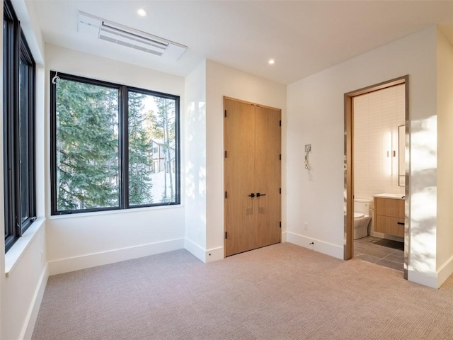 unfurnished bedroom featuring connected bathroom, multiple windows, and light carpet