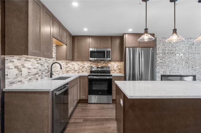 kitchen featuring sink, decorative light fixtures, dark hardwood / wood-style floors, stainless steel appliances, and light stone countertops