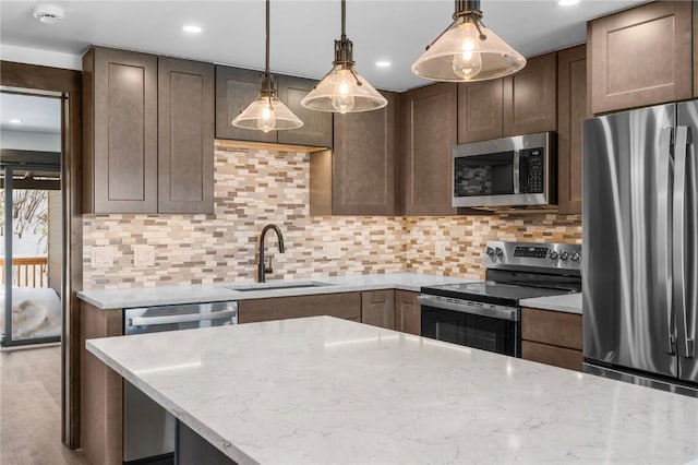 kitchen featuring sink, light stone counters, tasteful backsplash, appliances with stainless steel finishes, and pendant lighting