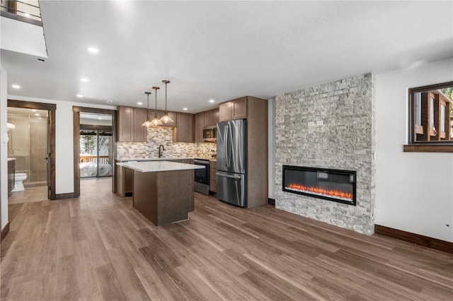 kitchen with a stone fireplace, appliances with stainless steel finishes, dark hardwood / wood-style floors, a center island, and decorative light fixtures