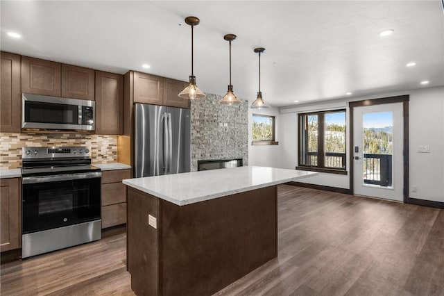 kitchen featuring dark hardwood / wood-style floors, pendant lighting, backsplash, a center island, and stainless steel appliances