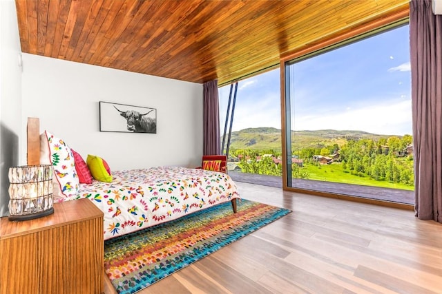 bedroom with a wall of windows, access to exterior, a mountain view, wooden ceiling, and light wood-type flooring