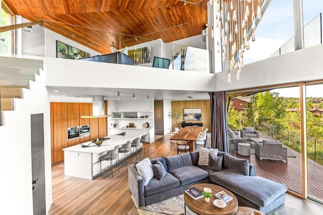 living area featuring wooden ceiling, rail lighting, light wood-type flooring, and a towering ceiling