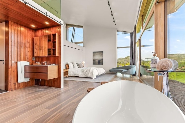 bedroom with multiple windows, hardwood / wood-style floors, wooden walls, and rail lighting