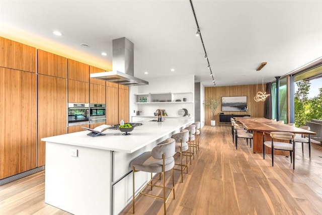 kitchen featuring rail lighting, wooden walls, extractor fan, a kitchen bar, and light wood-type flooring