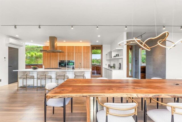 dining area featuring a wall mounted AC, sink, and light wood-type flooring